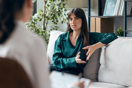 Shot of beautiful woman having therapy while the psychologist takes notes, sitting on the couch in the psychology office