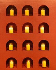 Symmetrical Grid of Lit Yellow Candles in Arched Terracotta Wall Niches with Warm Glow