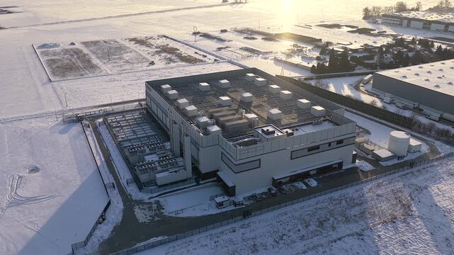 Orbiting aerial shot showcasing a large, modern data center building surrounded by snow covered fields during a cold winter day at sunset