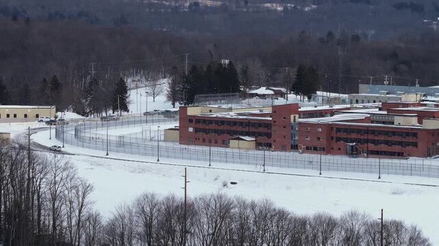 Aerial view of Federal Correctional Institution Loretto in Pennsylvania with perimeter fence, guard road and snow covered grounds in winter. Wide shot.