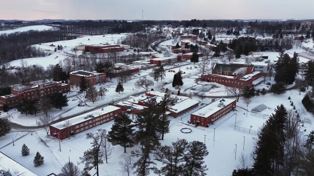 Aerial view of Saint Francis University campus in Loretto, Pennsylvania covered in snow with red brick academic buildings and winter landscape. Wide shot.