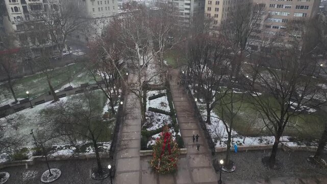 Aerial view of Rittenhouse Square park in Philadelphia during light snowfall with Christmas tree, winter park paths and people walking through historic city neighborhood. Tilt up. Snow rain in Philly.