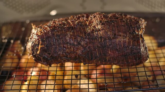 Close up of a seasoned beef roast sitting on a wire rack above roasted potatoes inside a hot oven.