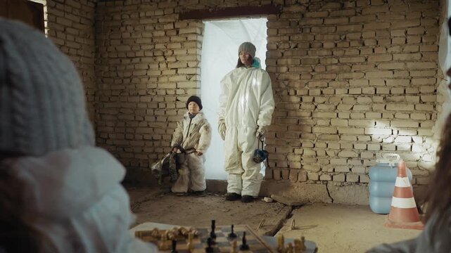 boy survivor brings scientist into abandoned brick shelter while other children watch from foreground, protective suits under dust lit window, fragile community rebuilding after postapocalypse