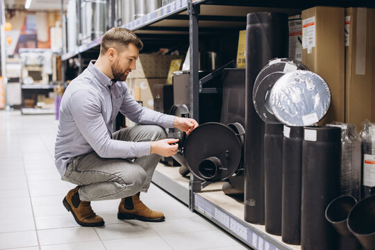 Man choosing heating and ventilation equipment in a hardware store, carefully examining a chimney component