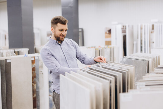 Man choosing ceramic flooring material for home renovation project in retail store showroom, comparing ceramic tiles samples