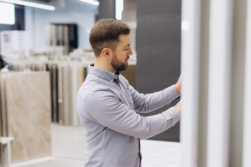 Fototapeta premium Man choosing new wall or floor tiles for home renovation project, selecting ceramic materials at a modern store