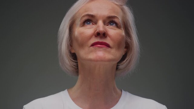 Portrait: close up view of face of elderly woman with blue eyes and wrinkled skin texture. Senior retired female, grey hair. Upper face of old caucasian person. Headshot, shirt, natural aging features