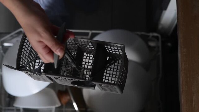 Top view close up of hands holding a cutlery container and removing clean spoons, forks, and knives. Overhead kitchen routine showing careful organization of tableware at home.