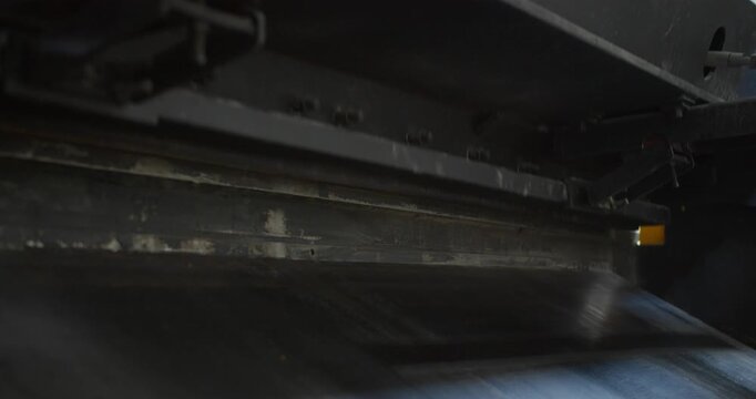 Cut metal falls behind an industrial guillotine shear during operation. Backside view of factory machine showing real-time metal cutting and blue collar production work