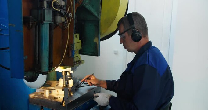 Press operator performing repetitive metal stamping task in factory, Routine industrial work and reliability of skilled production workers