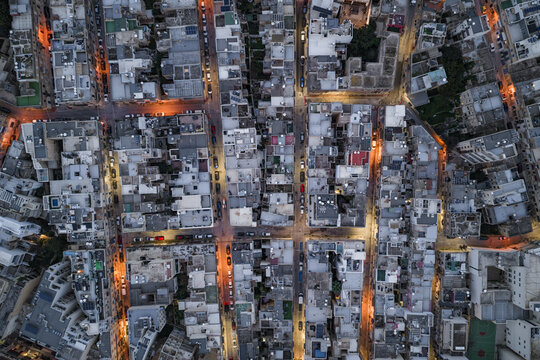 Aerial view of city streets aglow with warm light cutting through the cool tones of closely packed buildings, Sliema, Sliema, Malta.