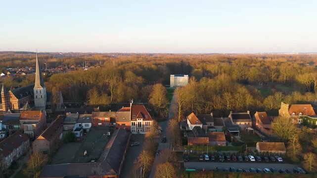 golden hour bornem church tall stone spire beside red roofed houses warm sunlight village wooded grounds d&rsquo;ursel castle near drone view belgium red-roofed 