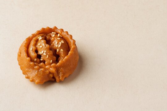 Traditional Moroccan chebakia pastry topped with sesame seeds, placed on a light beige background with copy space. Close-up, golden brown, syrup-glazed dessert.