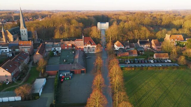 golden hour bornem village rooftops glowing beside tall church spire tree lined road leading through fields d&rsquo;ursel castle sunlit forest&rsquo;s edge reveals toward aerial view belgium 