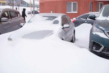 Cars covered in heavy snow in urban parking lot during winter storm