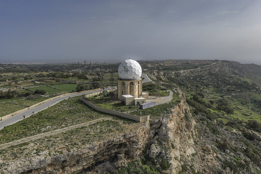 Aerial view of the Dingli Radar Station perched atop rugged cliffs, where the stark white dome contrasts with the island's earthy tones, Dingli, Malta.