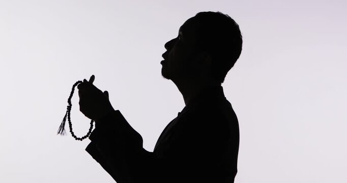 Silhouette of a Muslim Man Praying and Holding Misbaha Prayer Beads Against White Background