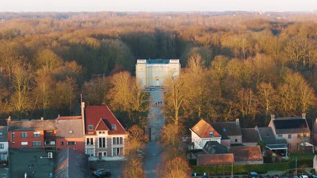 golden hour bornem looks straight tree lined avenue between warm toned village houses d&rsquo;ursel castle glowing edge dense forest toward down drone shot belgium tree-lined 