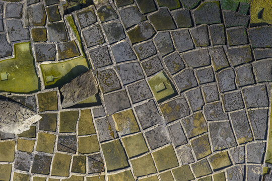Aerial view of the geometric patchwork of salt pans reflects the sky, creating a mosaic of cool blues, warm yellows, and earthy browns, Marsaskala, Malta.