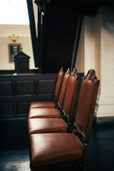 Obraz premium Row of empty vintage wooden chairs with leather seats inside a historic interior, soft light and shallow depth of field.