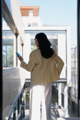 Fototapeta premium Woman holding phone looking at city view from balcony