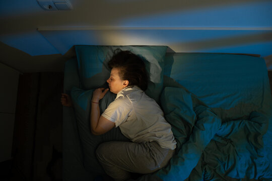 Top view of middle aged woman sleeping in fetal position on white bed at night