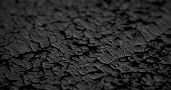 Macro Cracked Mud Texture on Black. Slow panning footage across a fissured dark surface, showcasing intricate polygonal crack patterns and rough granular details under subtle directional lighting.