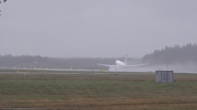 aircraft lifts off rain soaked runway oslo airport trailing heavy water spray climbs into dense mist dark forest line distance from norway gardermoen takeoff liftoff departure rotation 