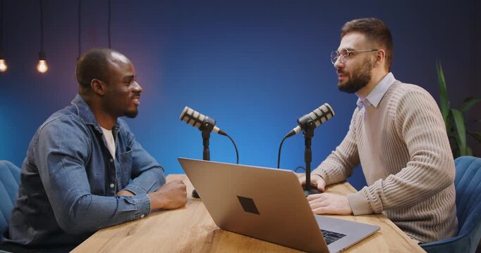 Podcasters giving a fist bump, celebrating a successful broadcast during an interview session with microphones and a laptop