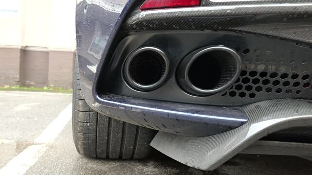 low rear detail focuses dual round exhaust outlets integrated into sculpted diffuser hexagonal venting carbon fiber accents rain marked blue paint angle tailpipes trim rain-marked bodywork 