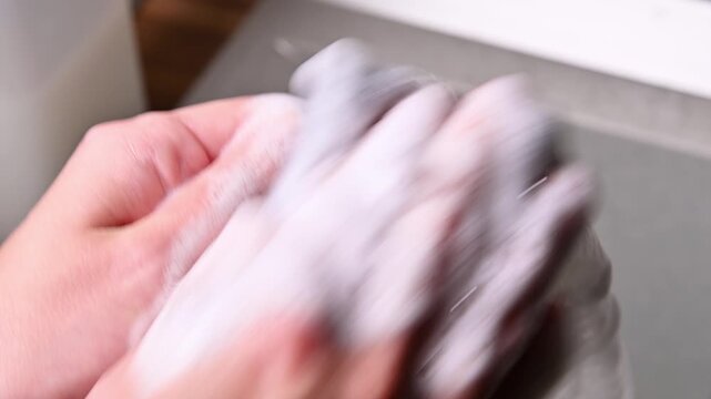 A close-up with localized lighting. The hands of a Caucasian woman washing dishes in a home kitchen late at night in the dark.