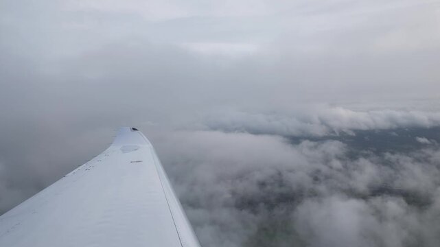 white aircraft wing slices through layered gray clouds breaks mist faint patchwork terrain below during calm overcast flight revealing far smooth sleek metal surface 