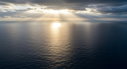Obraz premium Dramatic Cloudy Sky Over Peaceful Ocean Waters at Sunset with Shimmering Reflections and Rays of Sunlight Through Clouds