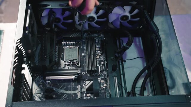Screwing bolt into motherboard during computer assembly process, close-up view focused on internal components of system unit
