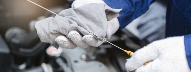 Close-up shot mechanician checking engine lubricant oil level at auto service station.