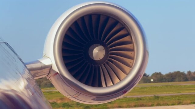 Closeup frontal view of a jet engine during the startup with the blades spinning, in a scene bathed in sunrise light.