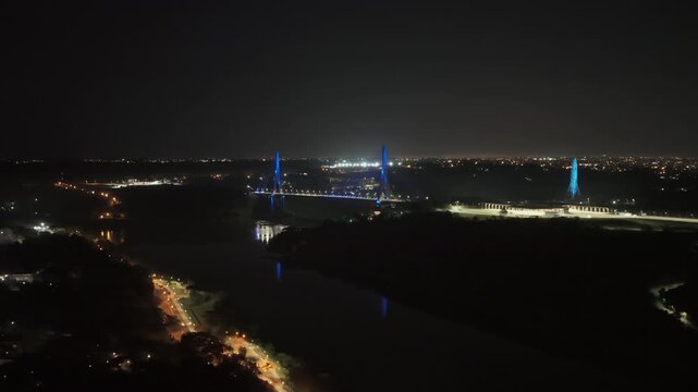 Night aerial view from Argentina of Integration Bridge lit blue over Parana River, with city lights and Avenida R&iacute;o de Iguazu