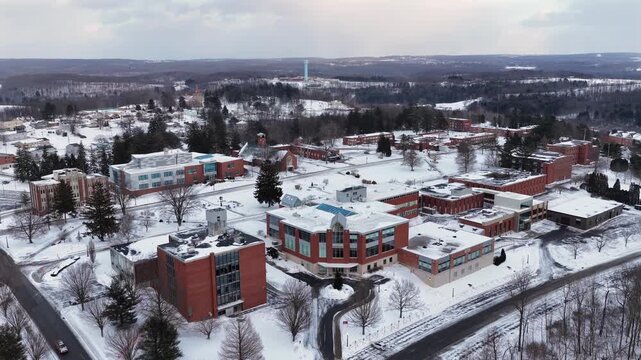 Red brick of historic Saint Francis University in loretto, Pennsylvania. Aerial wide shot. Snowy winter landscape in USA at sunset time. Rising shot.