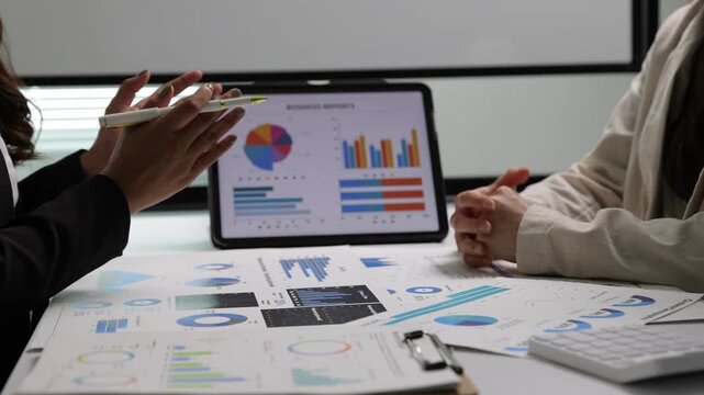 Businesswoman discussing financial data during a meeting. Financial advisors analyzing charts and graphs on a tablet and paper reports. Two colleagues working together on a business strategy.