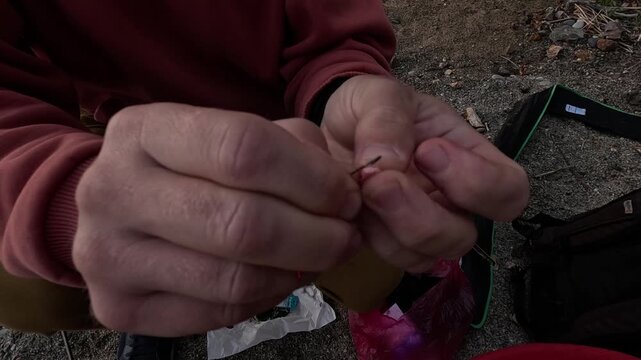 Fishing baiting hook, person preparing worm on fish hook outdoors, close up detail