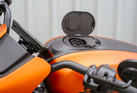 Open electric vehicle charging port on an orange motorcycle