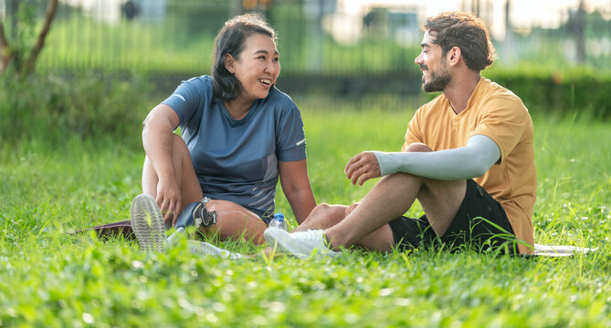 True friendship and equality happy woman with prosthetic leg relaxing on yoga mat with her supportive friend in park. Smiling female amputee with artificial limb enjoying with companion on grass.