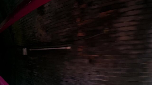 Handheld point of view moving through a dark, scary underground brick passageway lit by a single lamp