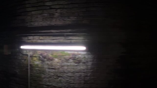 Handheld point of view moving through a dark, scary underground brick passageway lit by a single lamp