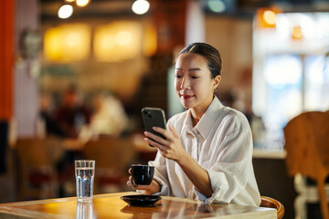 Woman drinking coffee and using smartphone in cafe