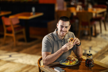 Young man enjoying lunch eating burger and fries in restaurant