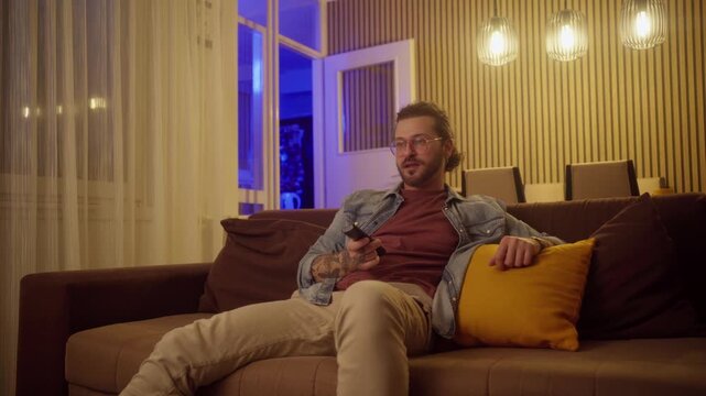 video of young man using remote controller while watching tv on couch