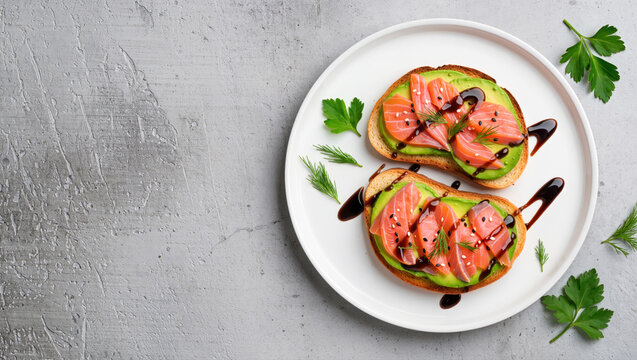 Avocado toast with salmon slices, sesame and balsamic glaze on white plate over gray concrete background