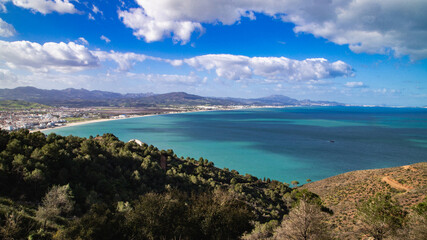 Panoramic view of M&rsquo;diq bay, wide beach, coastal town, mountains in the background and turquoise sea beneath a bright cloudy sky.
